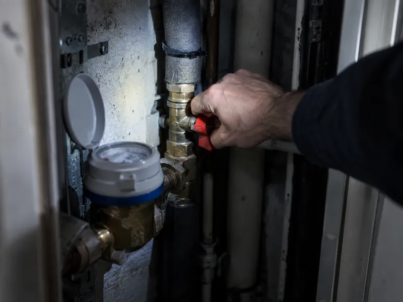 Main fermant la vanne d’arrêt près d’un compteur d’eau dans une gaine technique